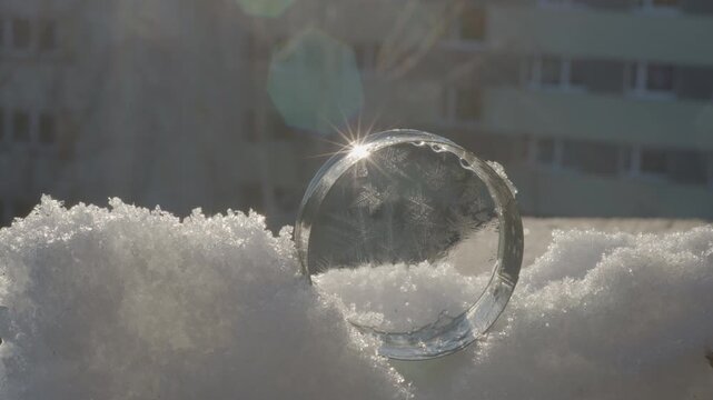 Video in subzero winter conditions where a hand places a circular soap filament on snow, capturing the freezing process and ice crystal formation in natural sunlight.
