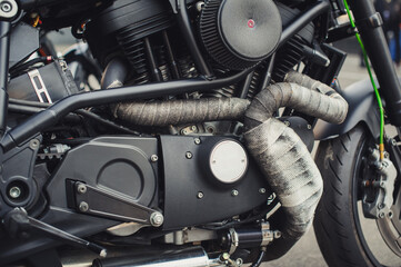Fototapeta premium Detailed shot of a powerful motorcycle engine and chassis. Highlights include exhaust pipes covered in grey thermal heat wrap, a black air filter intake, and various mechanical components.