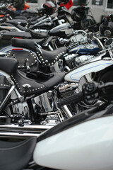 Obraz premium A high-angle, shallow depth-of-field shot showing a long line of parked classic motorcycles. The focus is on a black studded leather seat, chrome engine components, and a white fuel tank with blue pin