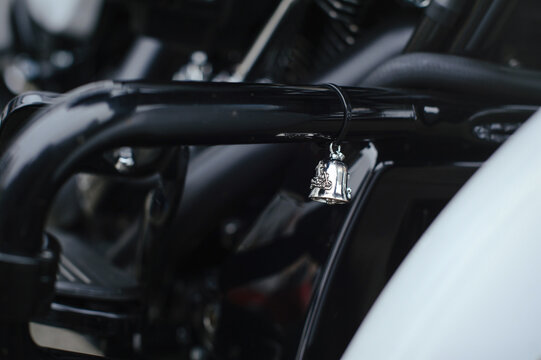 Detailed shot of a traditional silver "guardian bell" or "gremlin bell" with a motorcycle relief, attached to a black tubular motorcycle frame. Symbol of protection and good luck for bikers.