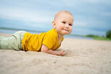 Fototapeta premium A happy toddler in a yellow shirt discovers the texture of sand on a bright beach day, embodying the wonder and excitement of exploring nature playground.