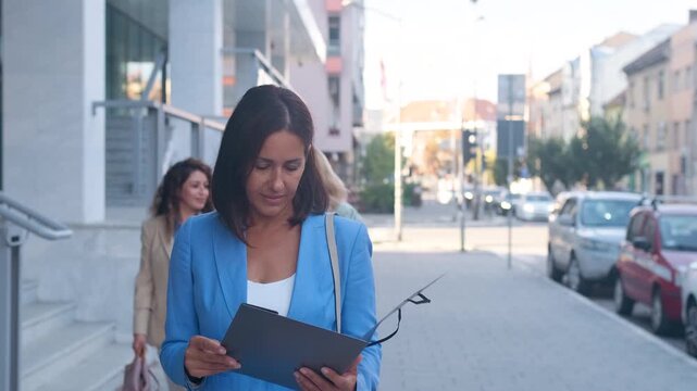 Businesswoman with folder walking in front of modern office building.