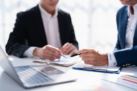 Business partners analyzing financial reports and strategizing solutions on documents with pens and a laptop during a meeting, focusing on collaboration and decision-making for growth