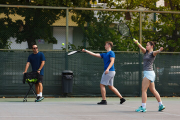 Obraz premium Tennis practice session with two players and a coach on an outdoor court during a sunny afternoon