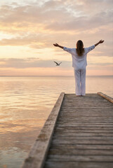 Fototapeta premium A woman finds peace and liberty as she stands on a wooden pier, embracing the freedom of the calm ocean.