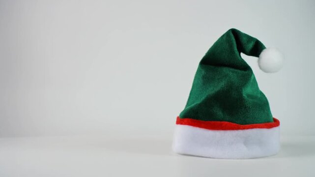 A green Christmas elf hat with red trim and white pompom on a white surface and background