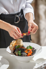 Woman opens mussel above seafood stew with bread and herbs