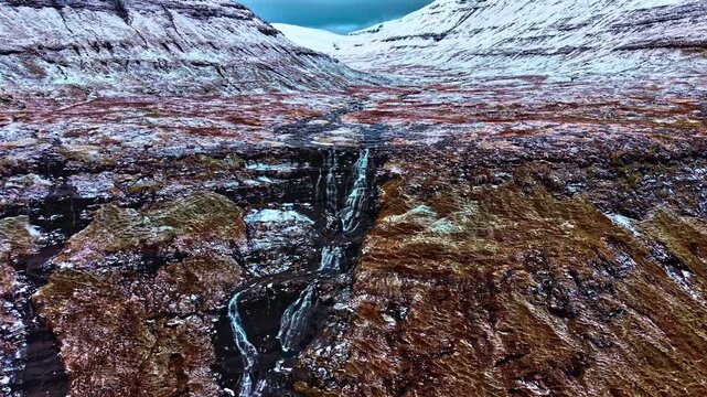 Aerial view of tiered waterfall in snowy Faroe Island landscape