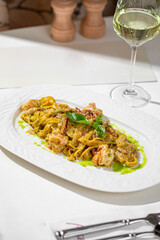 Pasta with shrimp served in creamy pesto sauce on white plate with wine glass