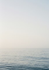 Obraz premium Expansive view of an empty ocean surface meeting a cloudless, pale sky, creating a minimalist, neutral backdrop for design or conceptual projects ,calm ,vast ,infinite