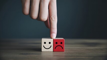 Finger pressing down on a sad face emoji block next to a happy face emoji block.