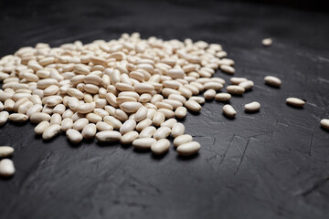 Fototapeta premium White beans scattered on a dark textured surface, showcasing their smooth, oval shapes and natural color variations in a close-up view