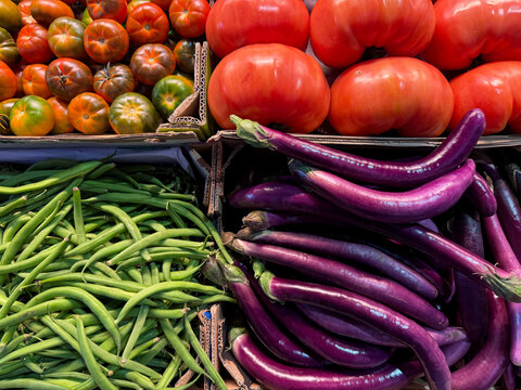Fresh assorted vegetables on the market, red tomatoes, purple long eggplants, green beans in boxes in grocery store high angle view