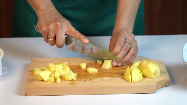 Woman Hand Dicing Raw Potatoes on Wooden Cutting Board