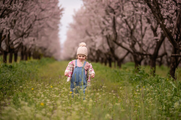 Little child happily exploring a blooming almond orchard on a spring day, smiling while walking through the green grass and wildflowers, connecting with nature and enjoying childhood