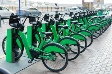 Obraz premium Row of green rental bikes parked at a docking station on a city street.