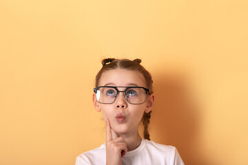 Young girl wearing glasses, looking up thoughtfully against a clean pastel yellow background. Ideal for education, imagination, and curiosity concepts.