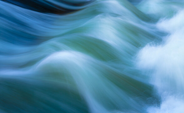 Fast-flowing water captured with long exposure. Colorful greenish, bluish structures, splashes, and reflections on the famous standing wave of the Eisbach in Munich's English Garden, a popular spot fo