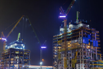 Cranes and scaffolding illuminate a building under construction at night.