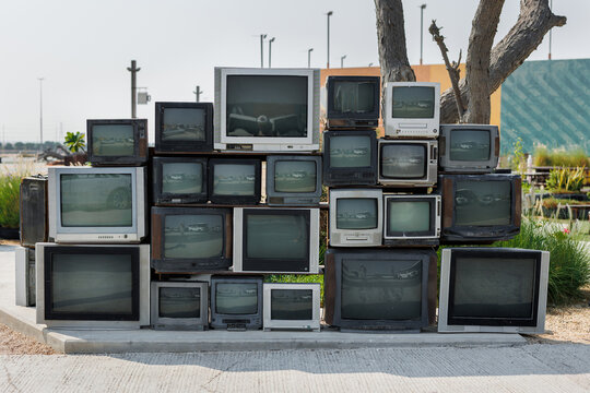 Pile of old cathode ray tube television sets stacked outdoors as art installation.