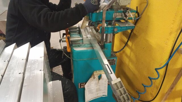 Milling hinge slots in aluminum profiles using an industrial cutting machine in a workshop.