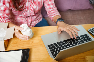 SME entrepreneur checking order on laptop while holding tea pot. Hand of female merchant preparing ceramic ware for shipping delivery. Online seller woman holding small white ceramic teapot.