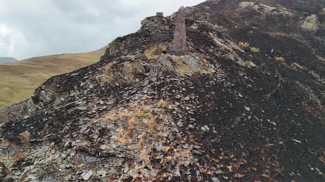 Cinematic aerial view of ruined mutso fortress watchtower on a burned hillside in the caucasus mountains, representing concepts of desolation and decay