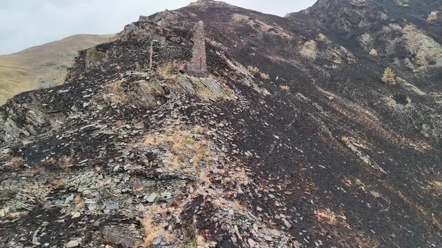 Drone flying over the historic ruins of the mutso fortress in georgia, with a scorched mountain landscape revealing the dramatic aftermath of a wildfire