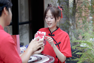 Obraz premium Surprised Asian woman in traditional Chinese red dress feels excited when received a gift from boyfriend. Woman with amazed expression looks at present gift box. Celebration Lunar Chinese New Year.