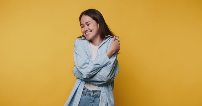 Smiling woman poses against yellow background while hugging herself during a photoshoot at a studio