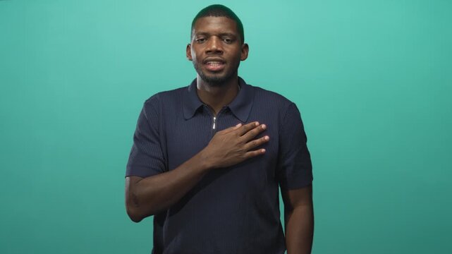 Man with hand pressed to chest and eyes closed in studio, standing in a pledge pose with palm contact and subtle expression; sincerity reflection.