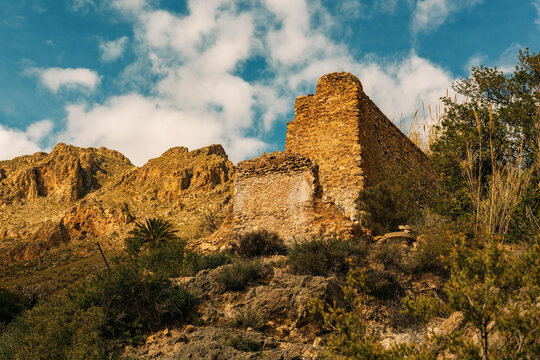 Ancient ruin of a mill on a steep rough rocky slope in mountainous landscape under blue sky with some clouds. Nijar, Almeria, Andalusia, Spain.