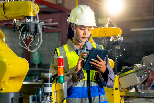 The engineer examines data on a tablet near the robot arm regarding industrial automated manufacturing processes technological safety devices and factory workflows.
