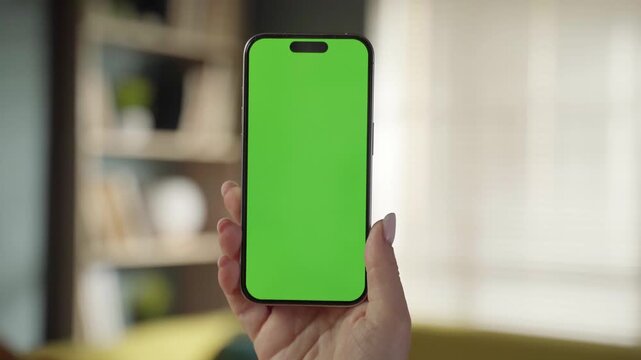 Person holding a mobile phone vertically with a customizable green screen, offering a digital template for displaying apps, content, and virtual experiences in a modern setting