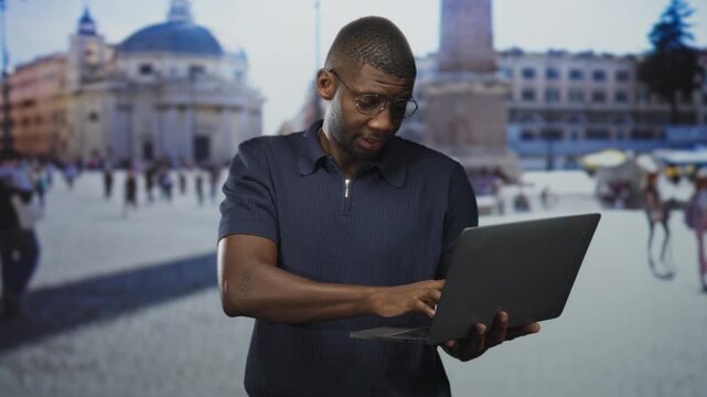 Man holding laptop with hand covering forehead in street plaza, facepalm gesture while viewing laptop screen; frustration problem solving.