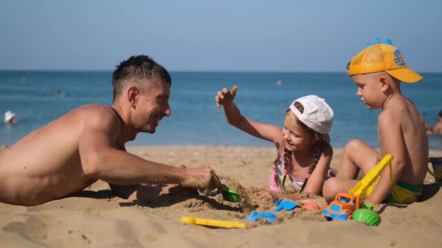 Father, son and daughter playing on the beach in the sand