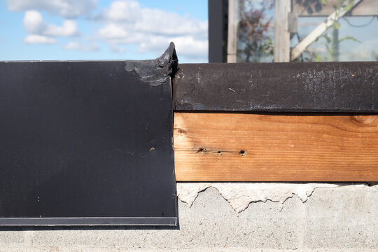 Roof metal flashing removed or blown off. Waterproofing flat roof or roof repair. Modified bitumen roofing membrane and wood section. Base sheet not covering to parapet wall topside. Selective focus.