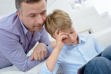 Obraz premium Man looking over shoulder of child using tablet