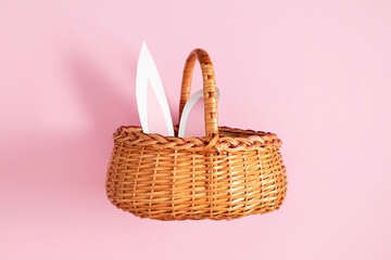 Empty natural wicker basket with handle and protruding rabbit ears standing on pink background. Spring, Easter shopping concept. Minimalism, bright colors