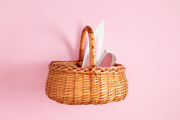 Easter basket. An empty wicker basket with a handle and protruding bunny ears, standing against a pink background. Spring and Easter shopping concept.