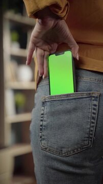 Person's hand pulling a modern smartphone with a bright green screen out of a blue jeans back pocket, ready for displaying custom content and advertising