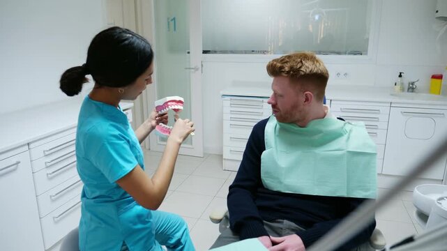 Female dentist teaching a male patient how to brush teeth using a jaw model and a toothbrush