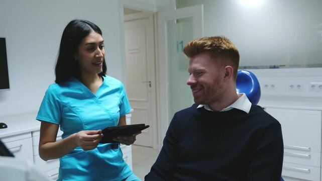 Dental assistant explaining the treatment to a male patient who signs the informed consent on a tablet