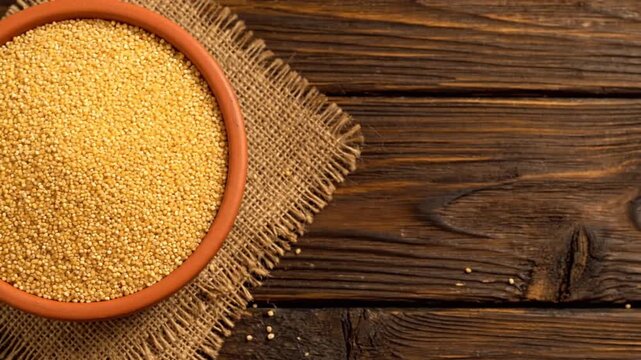 A terracotta bowl brimming with golden couscous or millet grains, resting on rustic burlap and a dark wooden table.