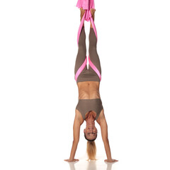 Studio shot of a smiling woman with blonde hair in a taupe sports outfit practicing aerial yoga in...
