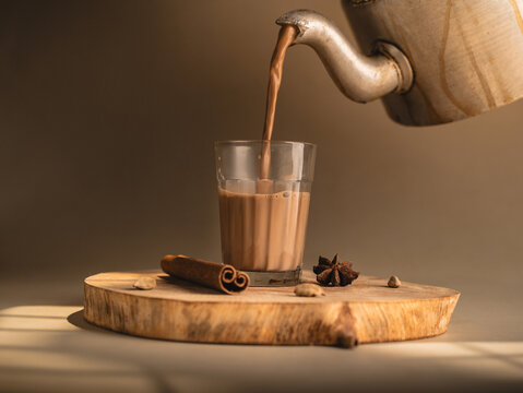 Indian chai served in glass cups, brewed in a metal kettle with aromatic masalas, getting poured on cup.
