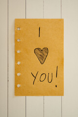 I love you, written on a piece of paper, on a white wooden background.