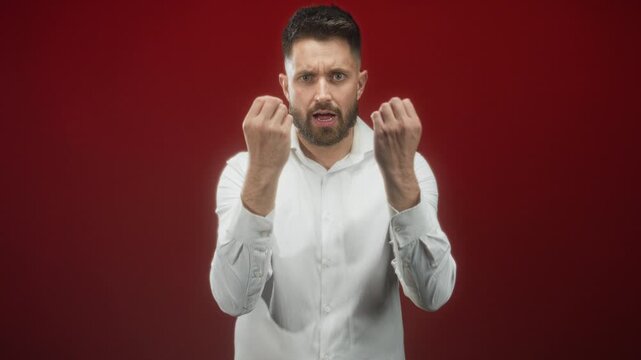 Hispanic man with beard and white shirt beckoning with fingers toward camera in red studio, expressive open hand gesture and intense gaze; demanding.