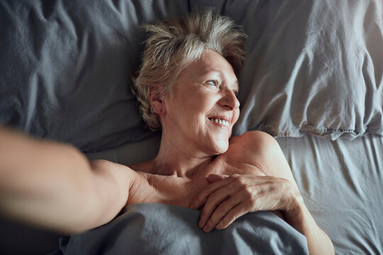 Smiling senior woman taking selfie in bed at home