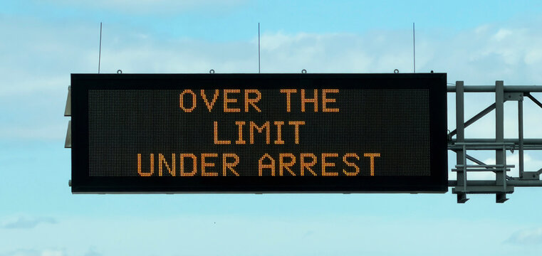 A bright electronic message board on a highway gantry warns drivers with the phrase 'Over The Limit Under Arrest', emphasizing road safety and DUI penalties, to reduce traffic violations.